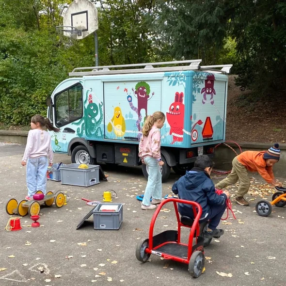 Ein bunt bemaltes Spielmobil-Auto mit spielenden Kindern.